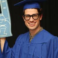 student in cap and gown holds up foam finger at GradFest